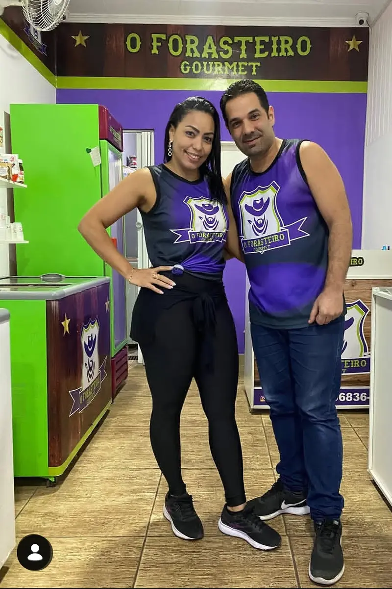 Os donos com a camisa roxa do Forasteiro, no salão com parede roxa, faixa verde e o nome da casa em letras douradas