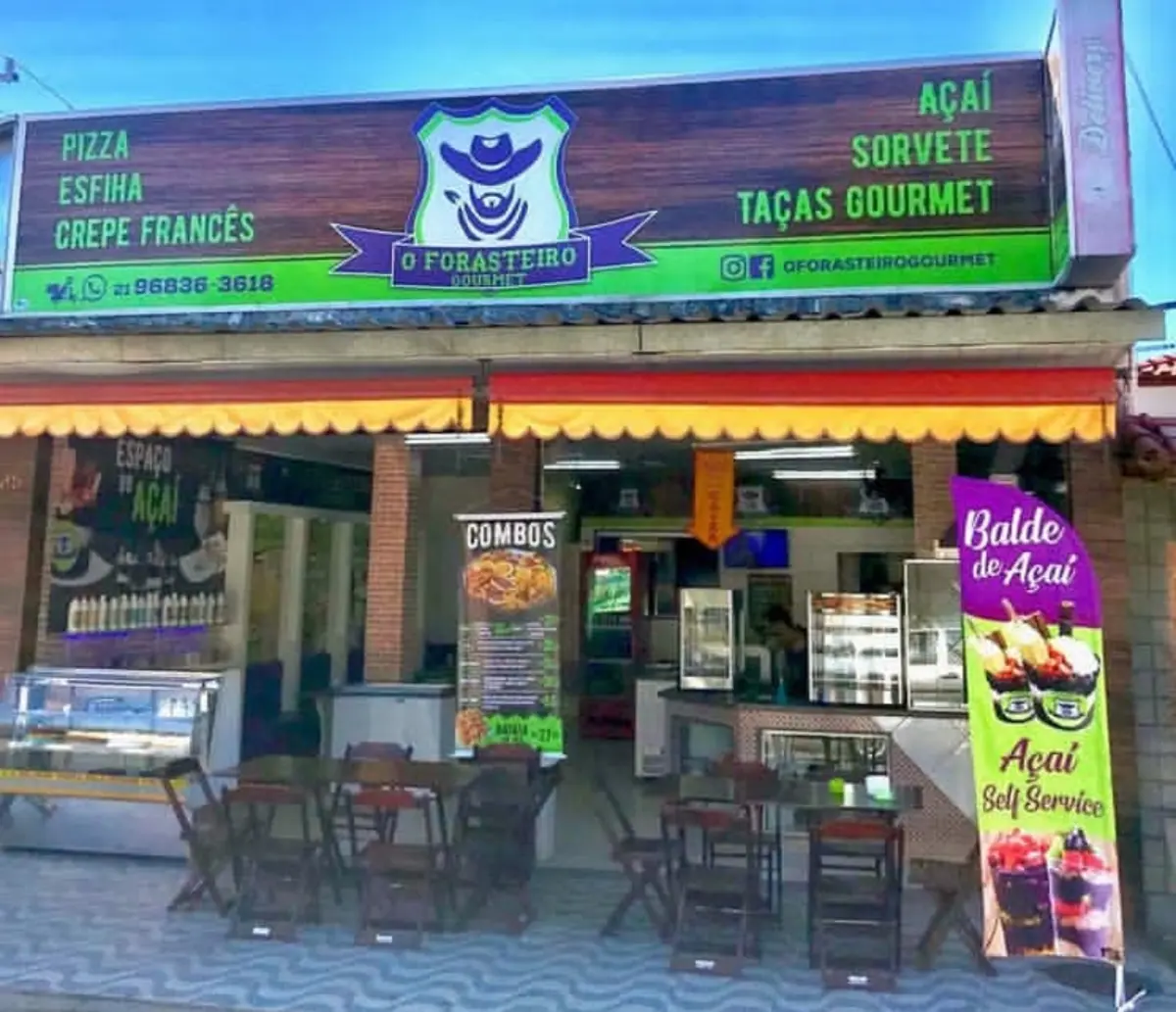 Fachada do Forasteiro Gourmet: letreiro de madeira com o escudo roxo, toldo amarelo, mesas na calçada e bandeira de balde de açaí